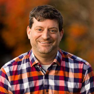 Jeff Witzel, a white man with short brown hair, wearing a plaid shirt smiling at the camera. 